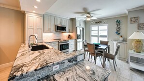 A kitchen with white cabinets, a granite countertop, a microwave, a refrigerator, and a ceiling fan.