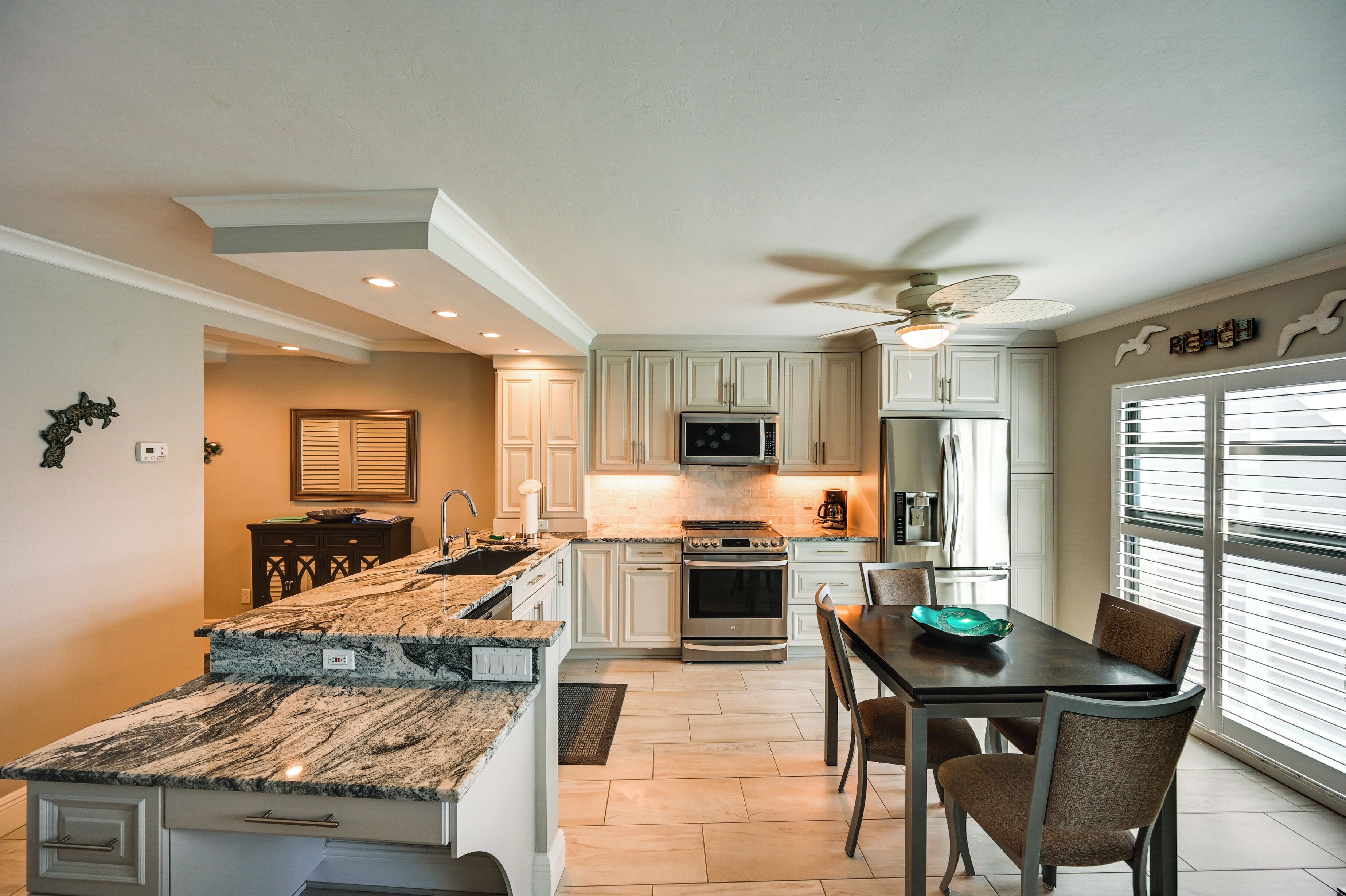 A modern kitchen with white cabinets, a granite countertop, and a dining area with a table and chairs.