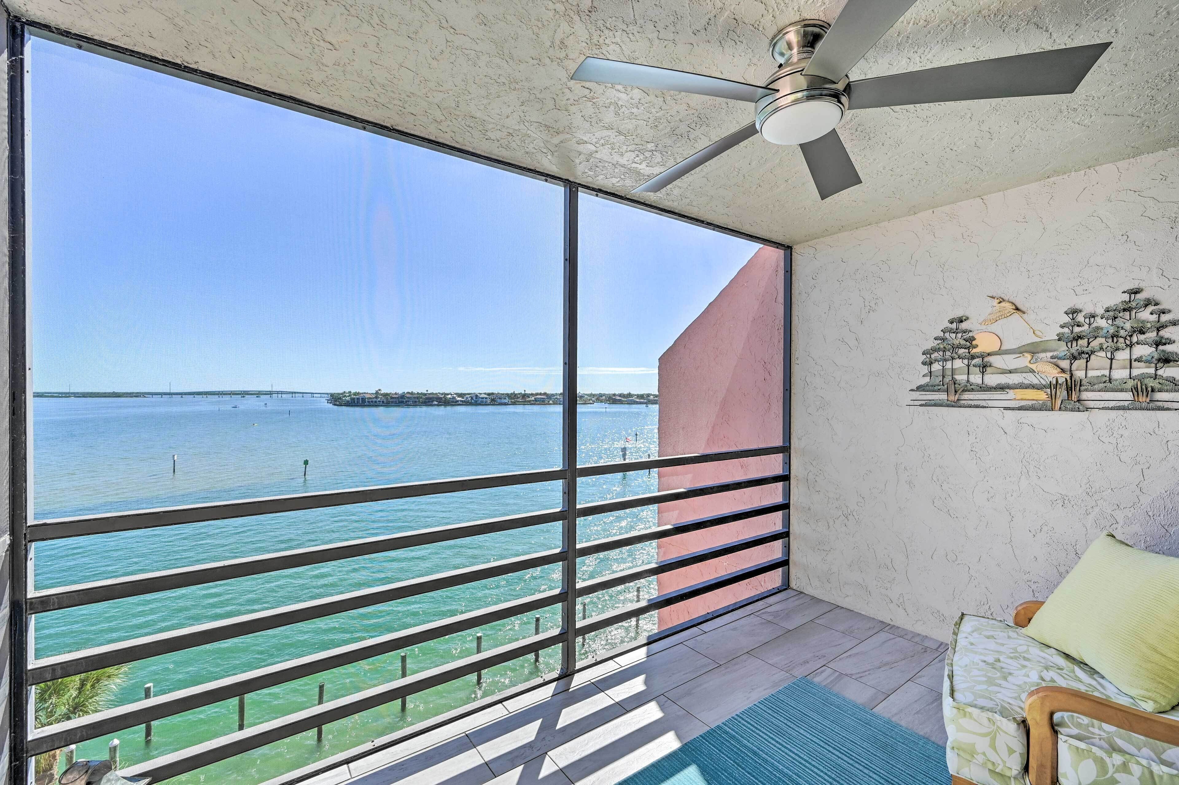 A balcony with a view of the sea, a ceiling fan, and a chair with a cushion.