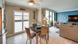 A modern living room with a dining area, a ceiling fan, and a large TV.