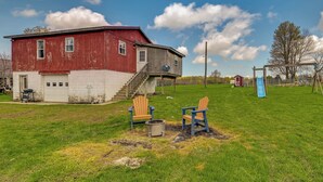 A red barn with a white lower section, a blue slide, and two Adirondack chairs on a grassy field. - Upstate New York Vacation Rental Near Cooperstown! (Jordanville)