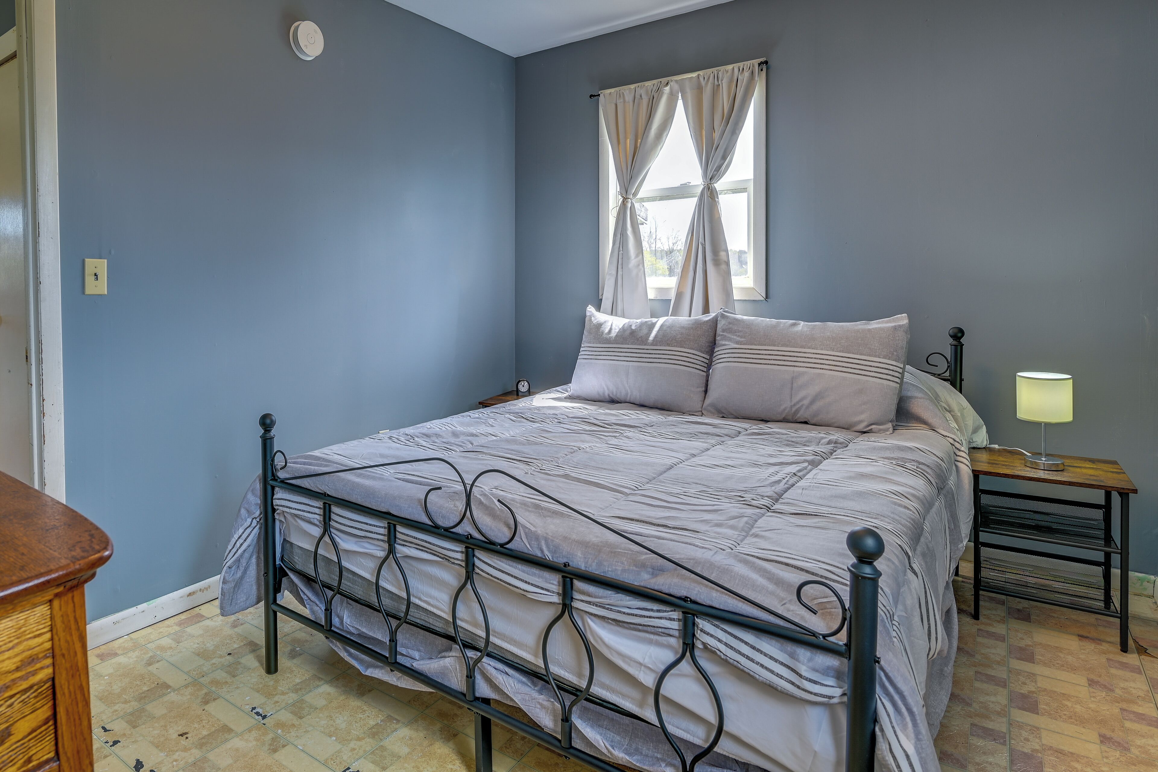 A bedroom with a bed, a nightstand, a lamp, and a window with curtains.