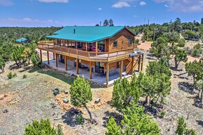 A wooden cabin with a green roof, a covered deck, and a dirt driveway surrounded by trees. - Overgaard Cabin w/ Pool Table & Incredible View (Overgaard)