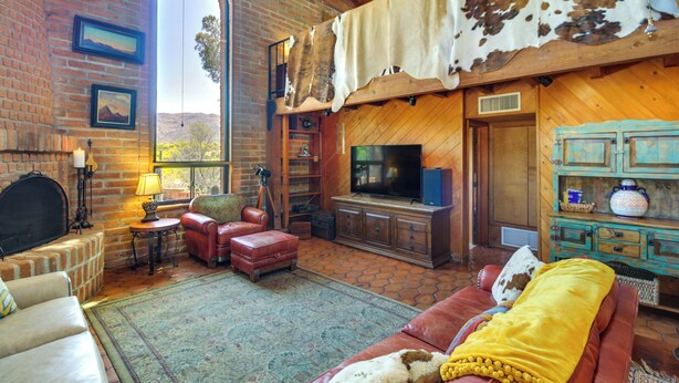 A rustic living room with a brick fireplace, leather furniture, a large flat-screen TV, and a cowhide hanging from the ceiling. - Eclectic Tucson Home 2 Mi to Saguaro National Park (Tucson)