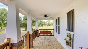 A covered porch with a wooden floor, a red bench, a ceiling fan, and a view of a green landscape. - New Bern Vacation Rental on Farm w/ Fire Pit! (New Bern)
