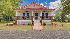 A two-story house with a red roof and white siding, a front porch with a brick column, and a small front yard with trees and shrubs. - New Bern Vacation Rental on Farm w/ Fire Pit! (New Bern)