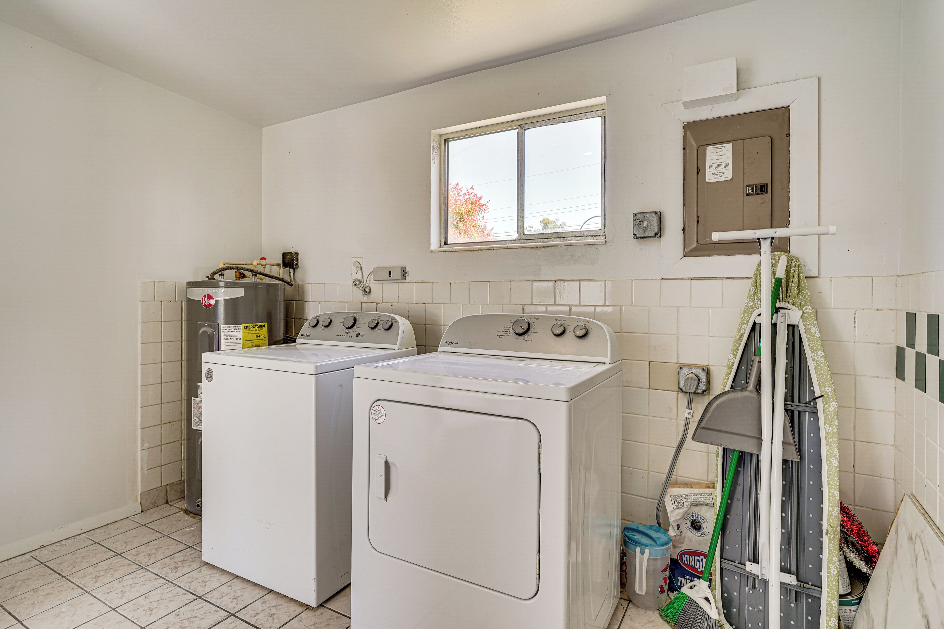 A laundry room with two white front-loading washers and dryers, a window, and a utility box on the wall.
