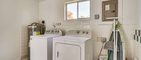 A laundry room with two white front-loading washers and dryers, a window, and a utility box on the wall.