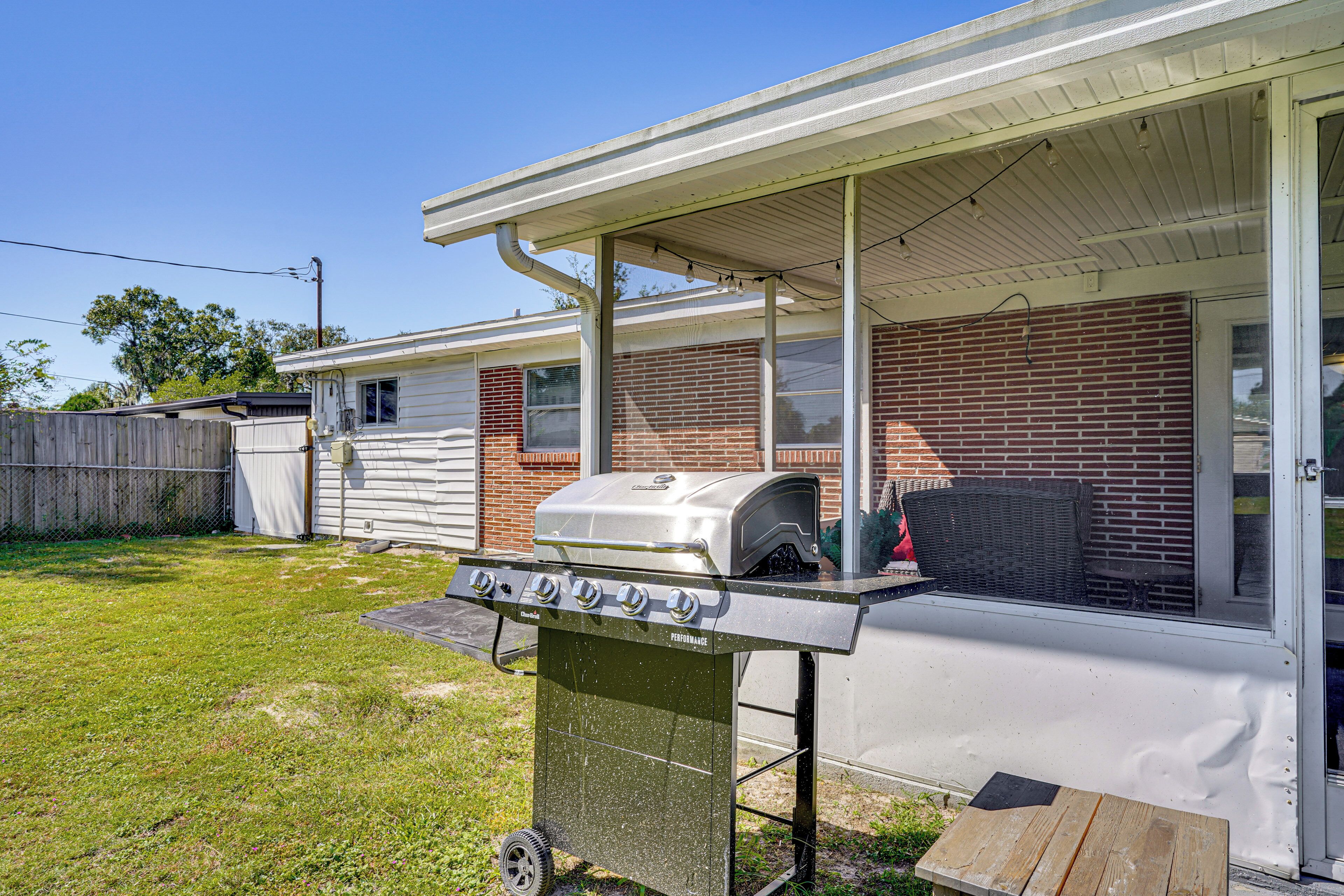 A backyard with a barbecue grill, a covered patio, and a brick house.