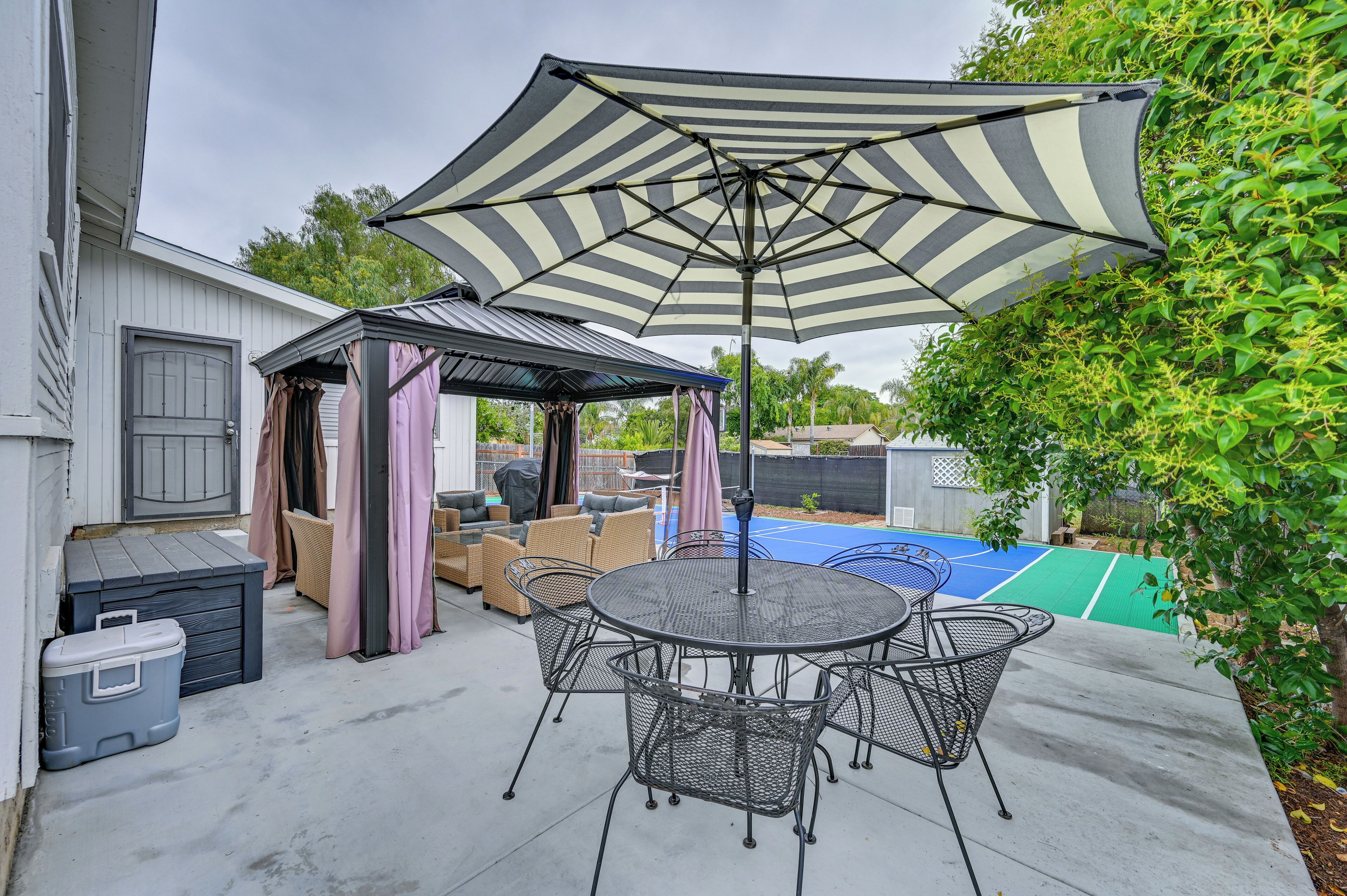A patio with a round table and chairs, a striped umbrella, and a covered seating area.