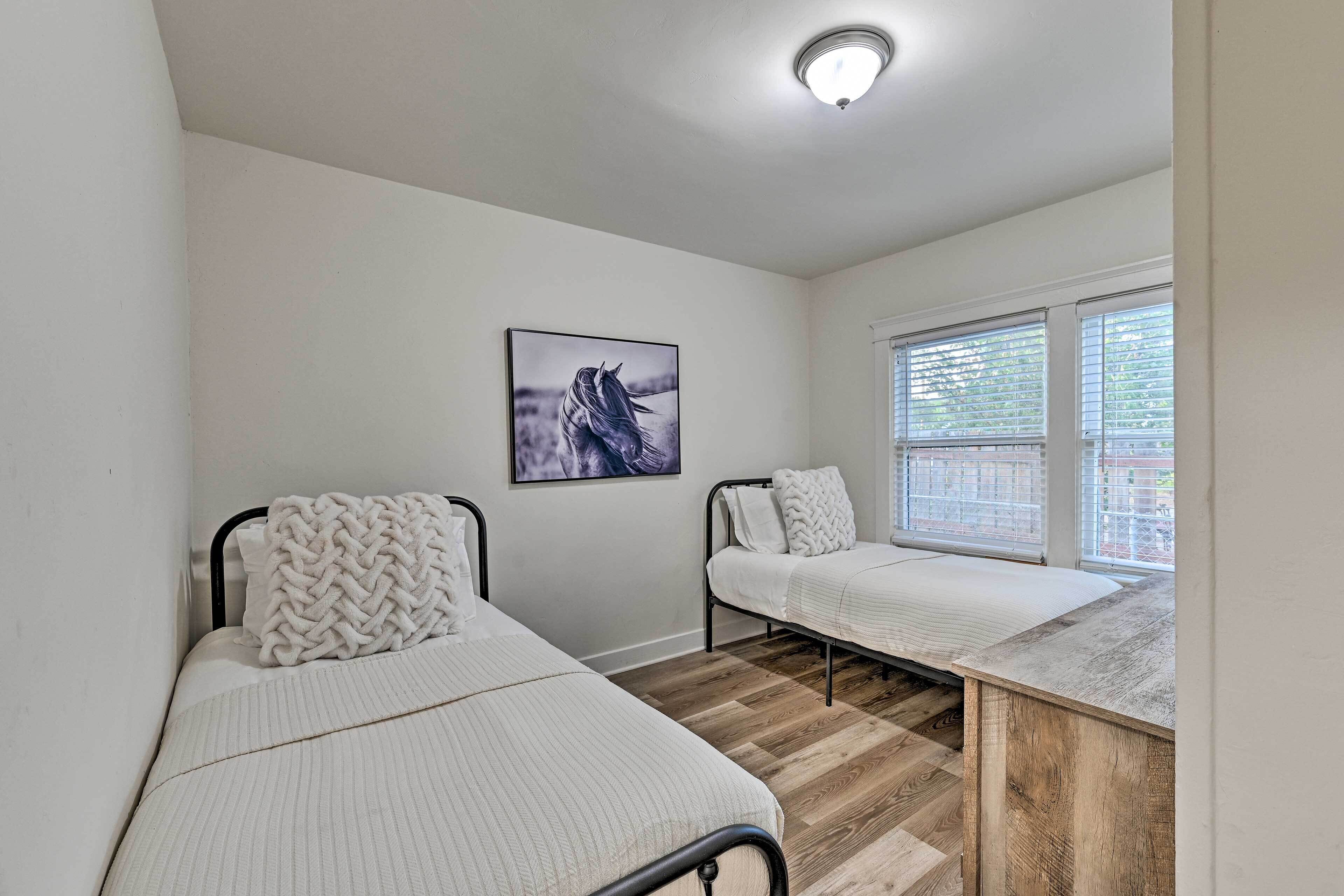 Une chambre avec deux lits, un bureau en bois, une fenêtre avec des stores et un luminaire au plafond.