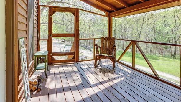 A wooden deck with a rustic chair and a small table, overlooking a forested area.