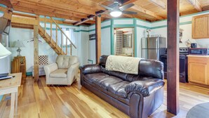 A spacious living room with a leather sofa, a wooden staircase, and a kitchen area with modern appliances.