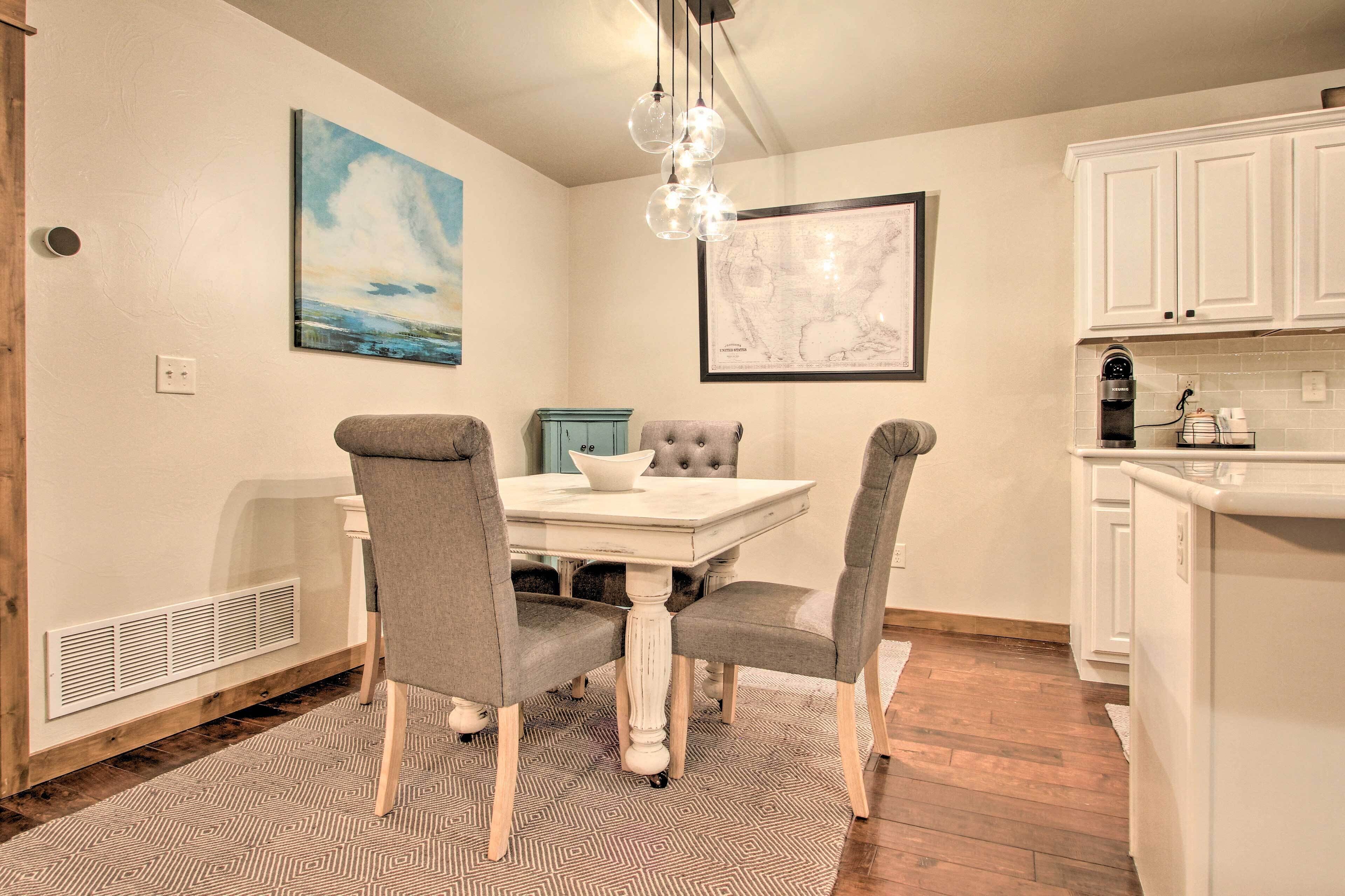 A dining area with a white table, grey upholstered chairs, a patterned rug, a painting, and a map on the wall.