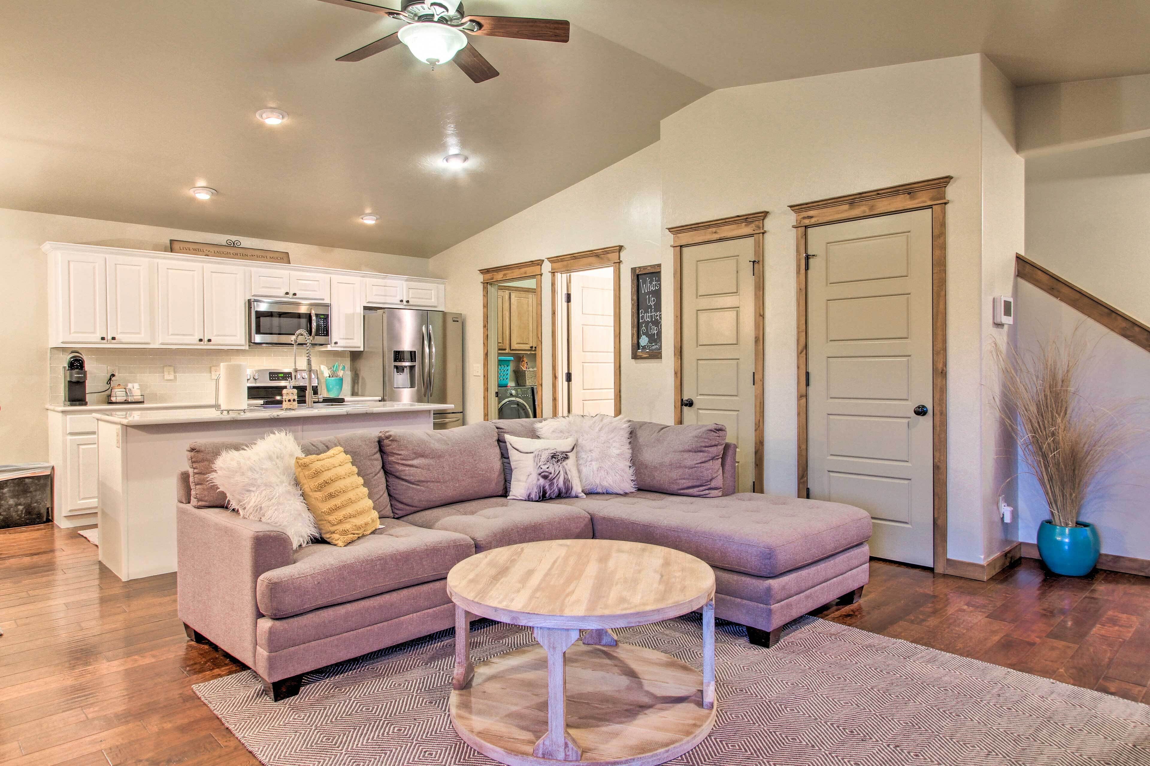 A living room with a sectional sofa, a round coffee table, and a kitchen in the background.