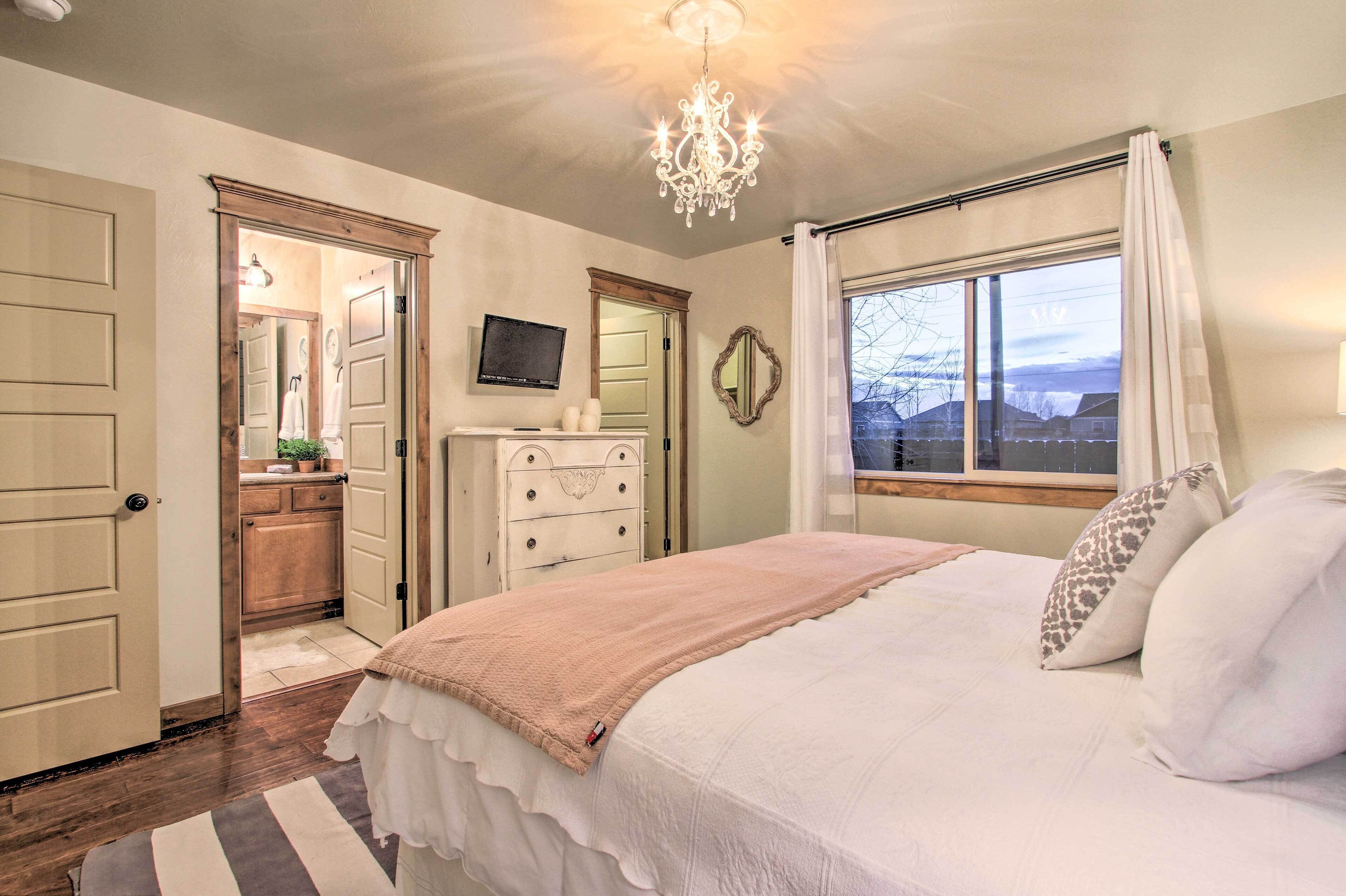 Un dormitorio con cama, cómoda, televisor y ventana con cortinas.