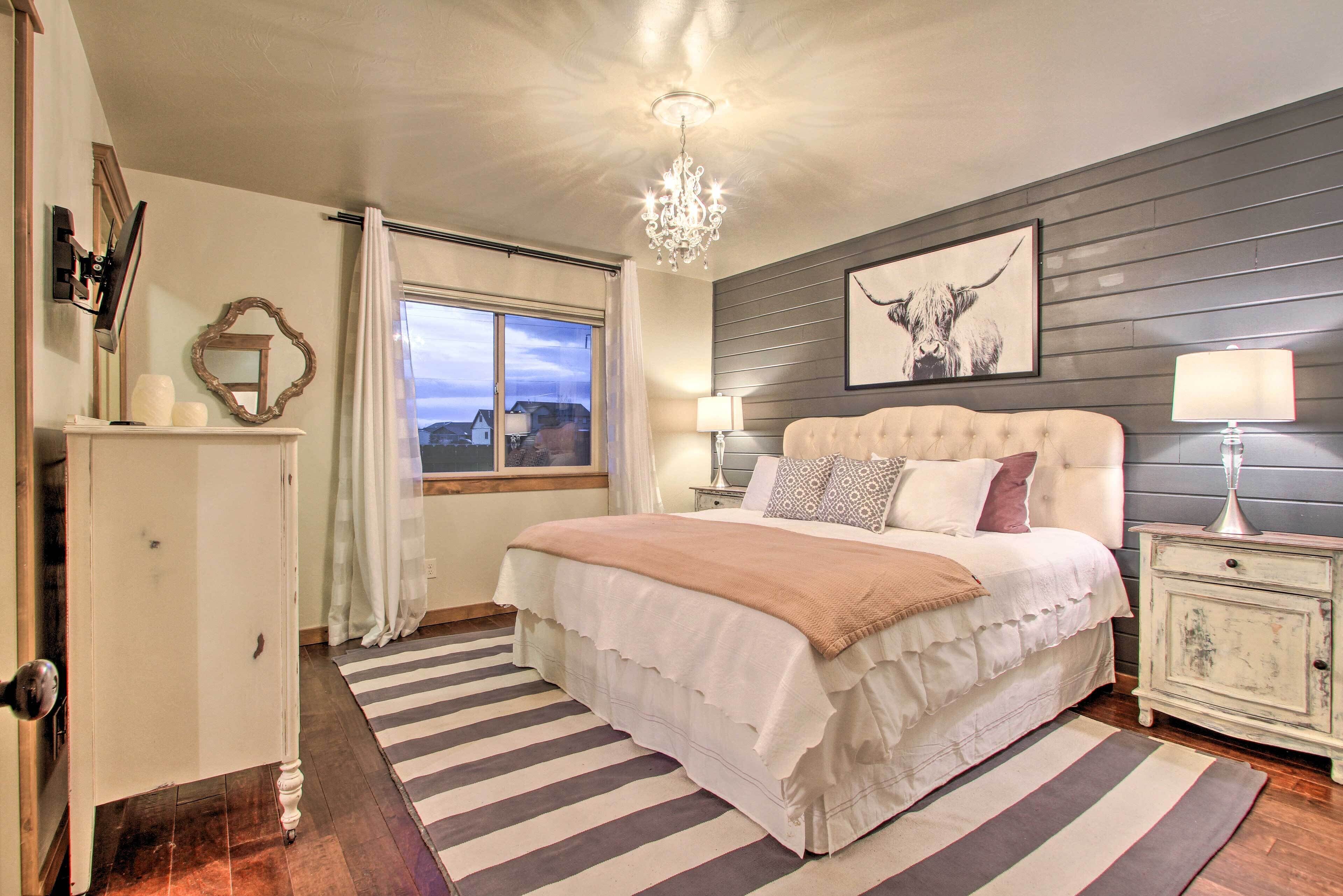 A bedroom with a large bed, a chandelier, a framed artwork, and a window with curtains.