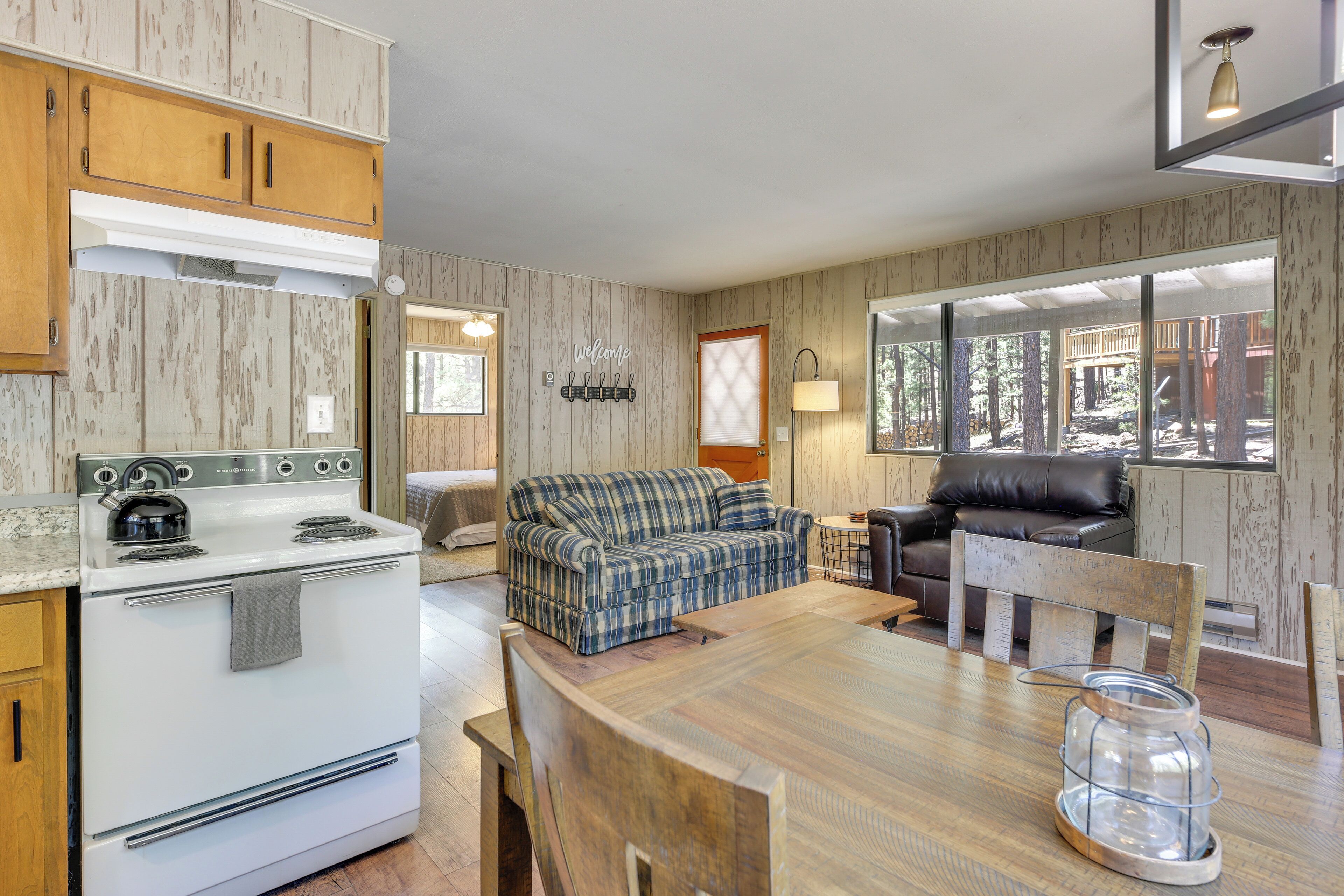 A compact kitchen with a stove, a dining table with chairs, a sofa, and a leather chair.