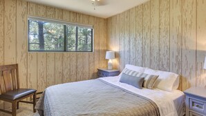 Quarto com cama grande, cadeira, mesa de cabeceira com abajur, e janela com vista para árvores.