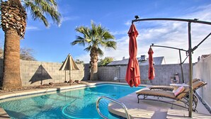A swimming pool with lounge chairs and umbrellas, surrounded by palm trees and a brick wall. - Glendale Oasis w/ Fenced Yard & Private Pool! (Glendale)