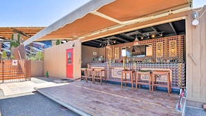 Un área de bar al aire libre con una terraza de madera, taburetes de bar y una pared repleta de botellas de licor.