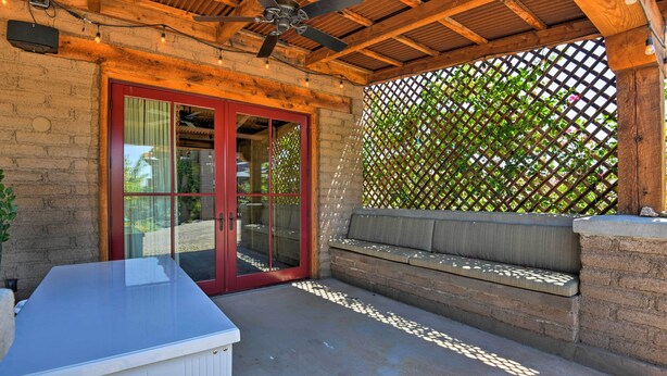 Un patio techado con una puerta de vidrio de marco rojo, piso de concreto y un banco de madera.