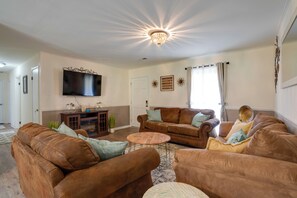 A living room with brown leather sofas, a wooden coffee table, a flat-screen TV mounted on the wall, and a chandelier. - Decatur Vacation Rental Retreat w/ Private Yard! (Decatur)