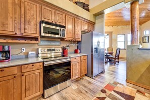 A kitchen with wooden cabinets, stainless steel appliances, and a patterned rug. - Luxe Resort Cabin w/ Deck: Hike, Swim, Relax! (Show Low)