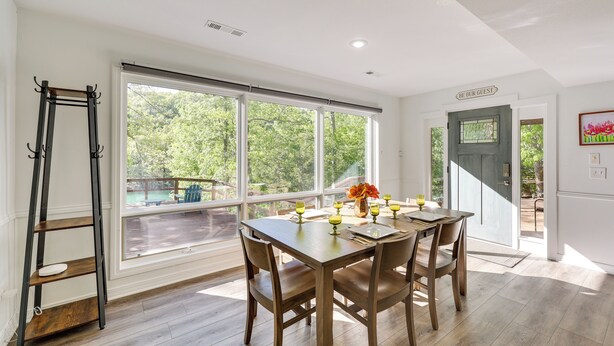Un coin repas avec une grande fenêtre, une table dressée pour quatre personnes et une échelle appuyée contre le mur.