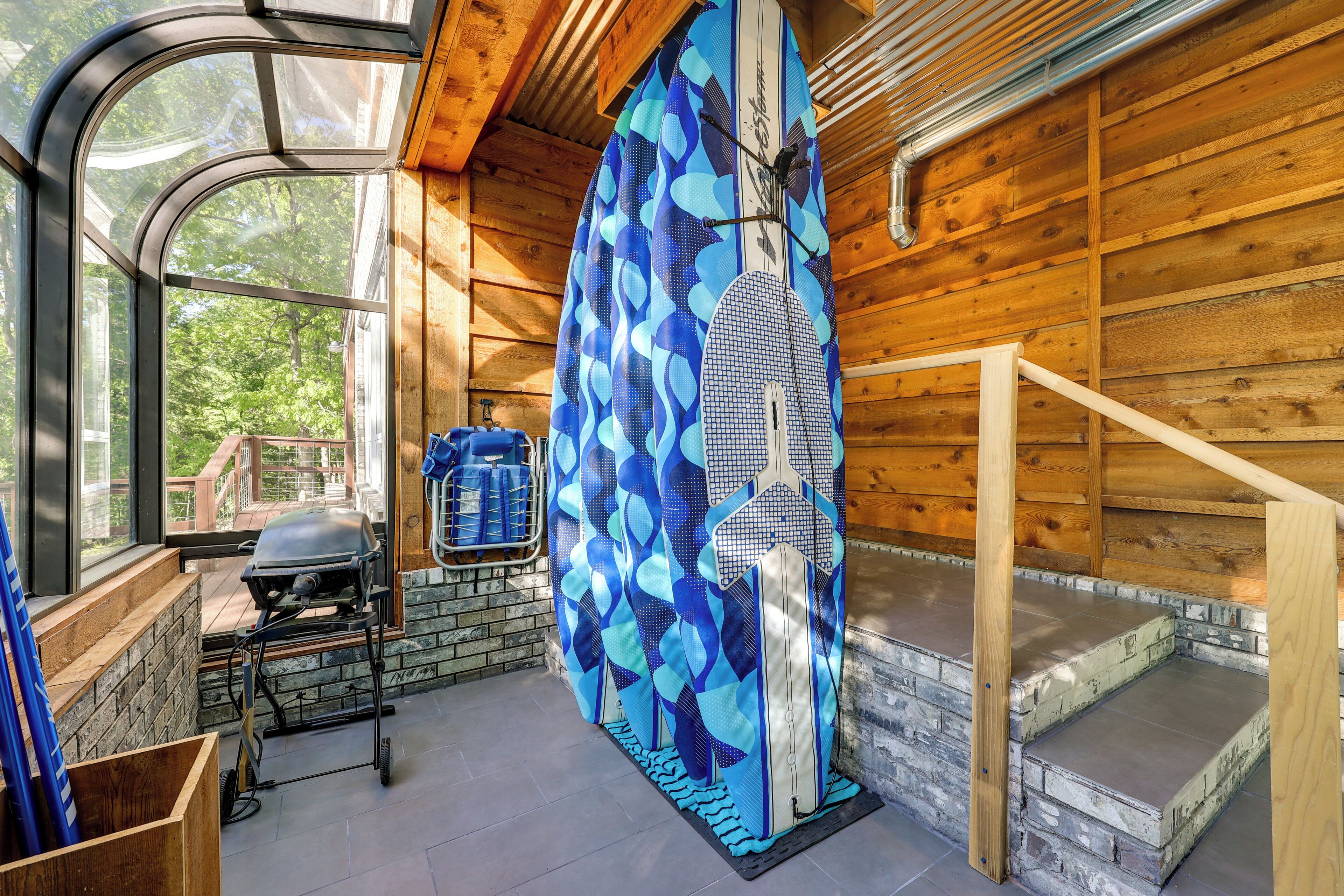 A wooden cabin interior with a large window, a grill, a patterned curtain, and a staircase.
