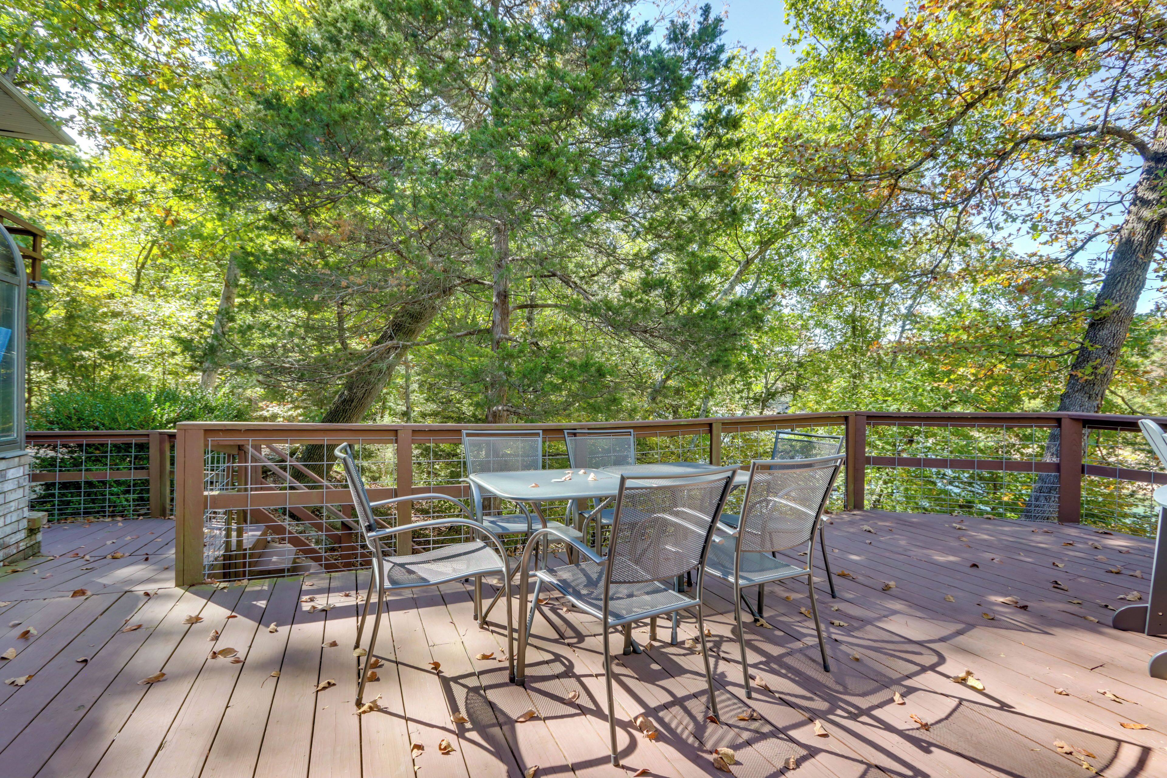 A wooden deck with metal chairs and a table, surrounded by trees.