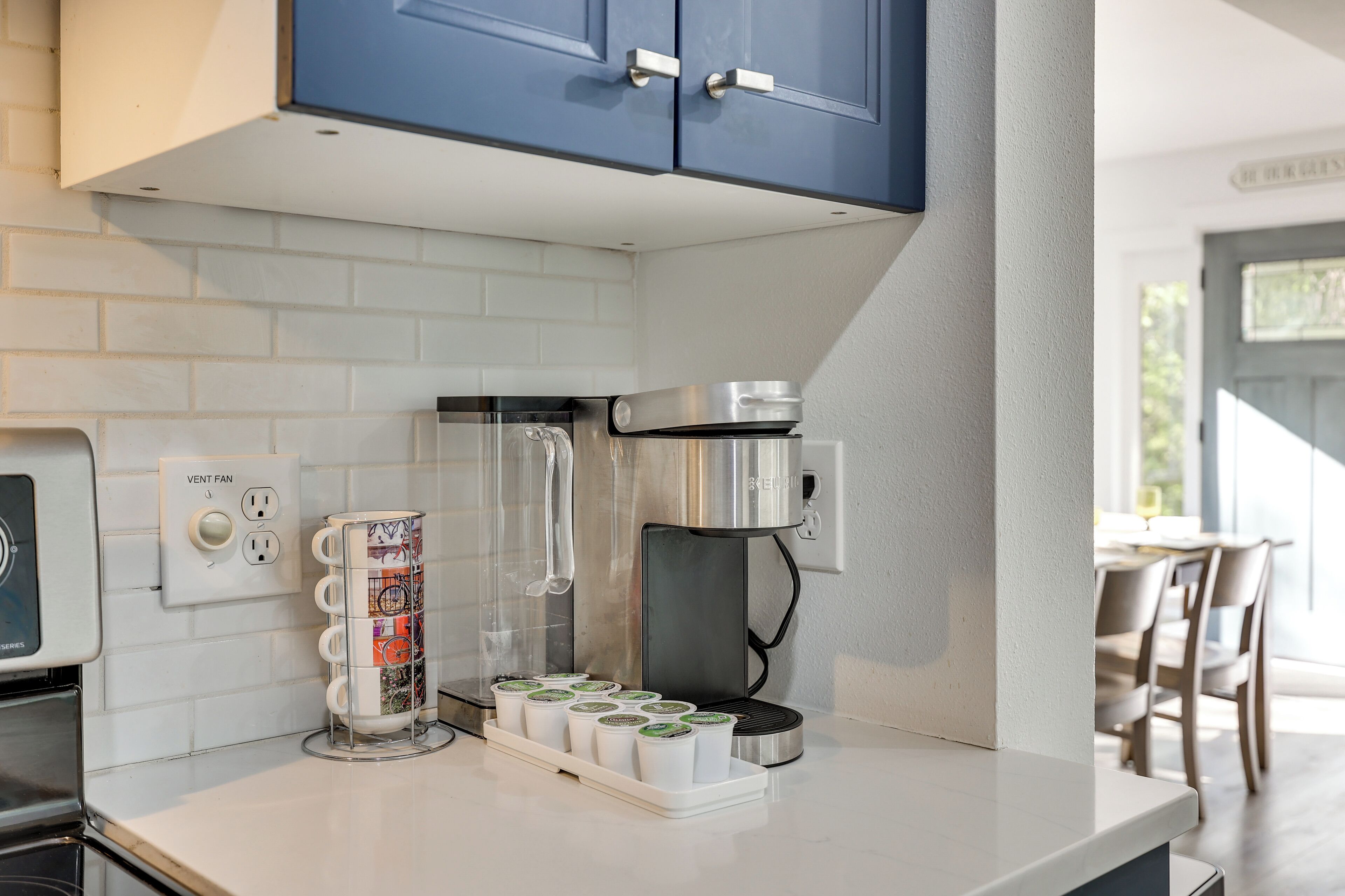 A kitchen with a coffee maker, a vent fan, and a coffee pod dispenser.