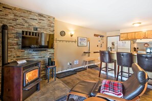Un salon chaleureux avec un mur en pierre, une cheminée, des fauteuils en cuir et un téléviseur.