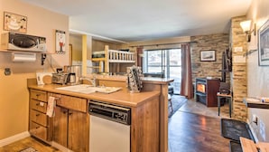 A compact kitchen with a built-in dishwasher, a microwave, and a coffee maker. There is a stone wall and a fireplace in the background. - Walk to Ski Lift & Village: Lovely Kirkwood Condo! (Kirkwood)