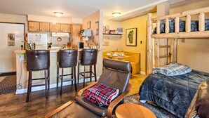 A compact living space with a kitchenette, a dining area, a lounge chair with a plaid blanket, and a bunk bed with a blue blanket. - Walk to Ski Lift & Village: Lovely Kirkwood Condo! (Kirkwood)