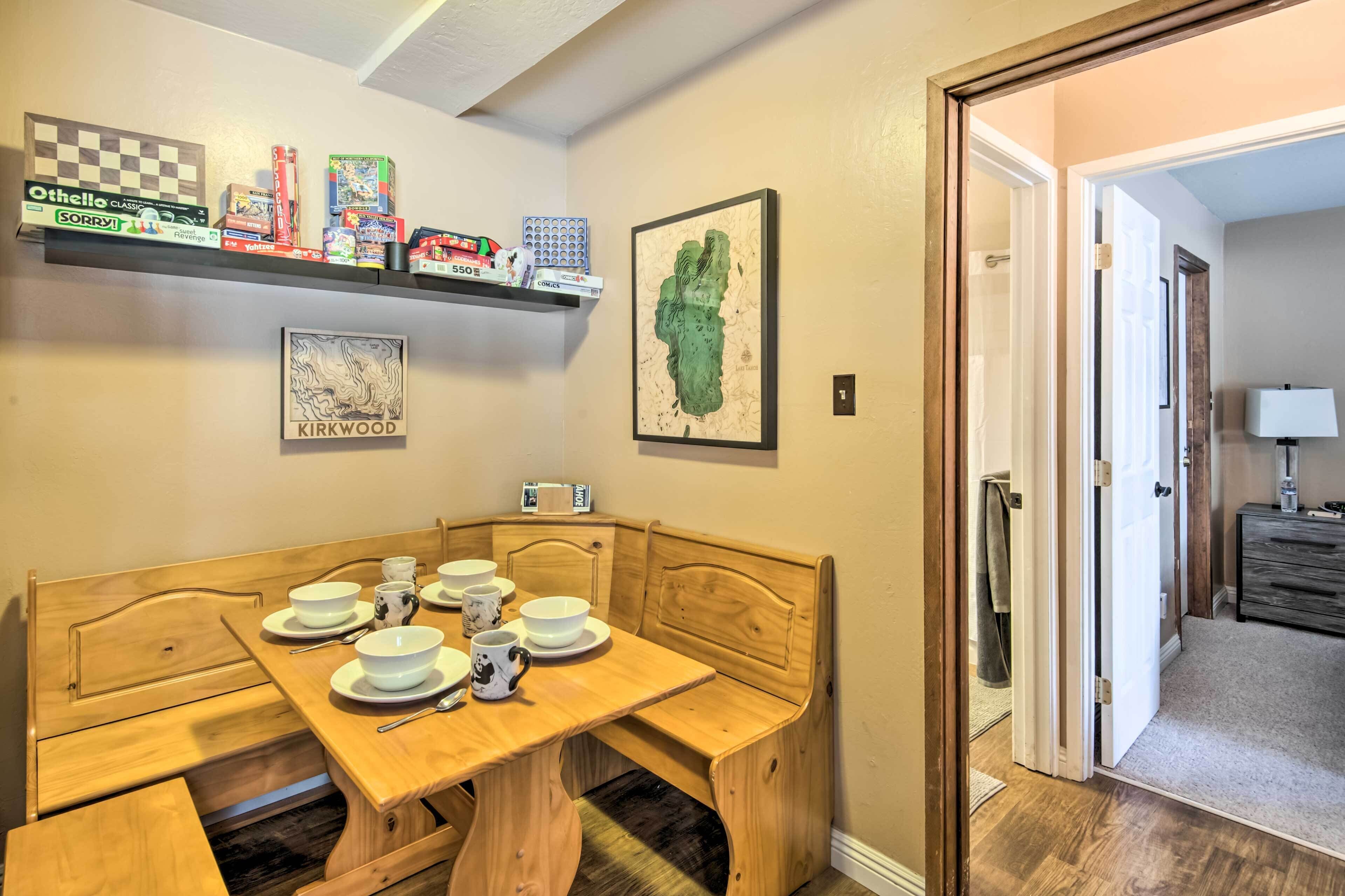 A dining area with a wooden table and bench, a shelf with board games, and a framed map on the wall.