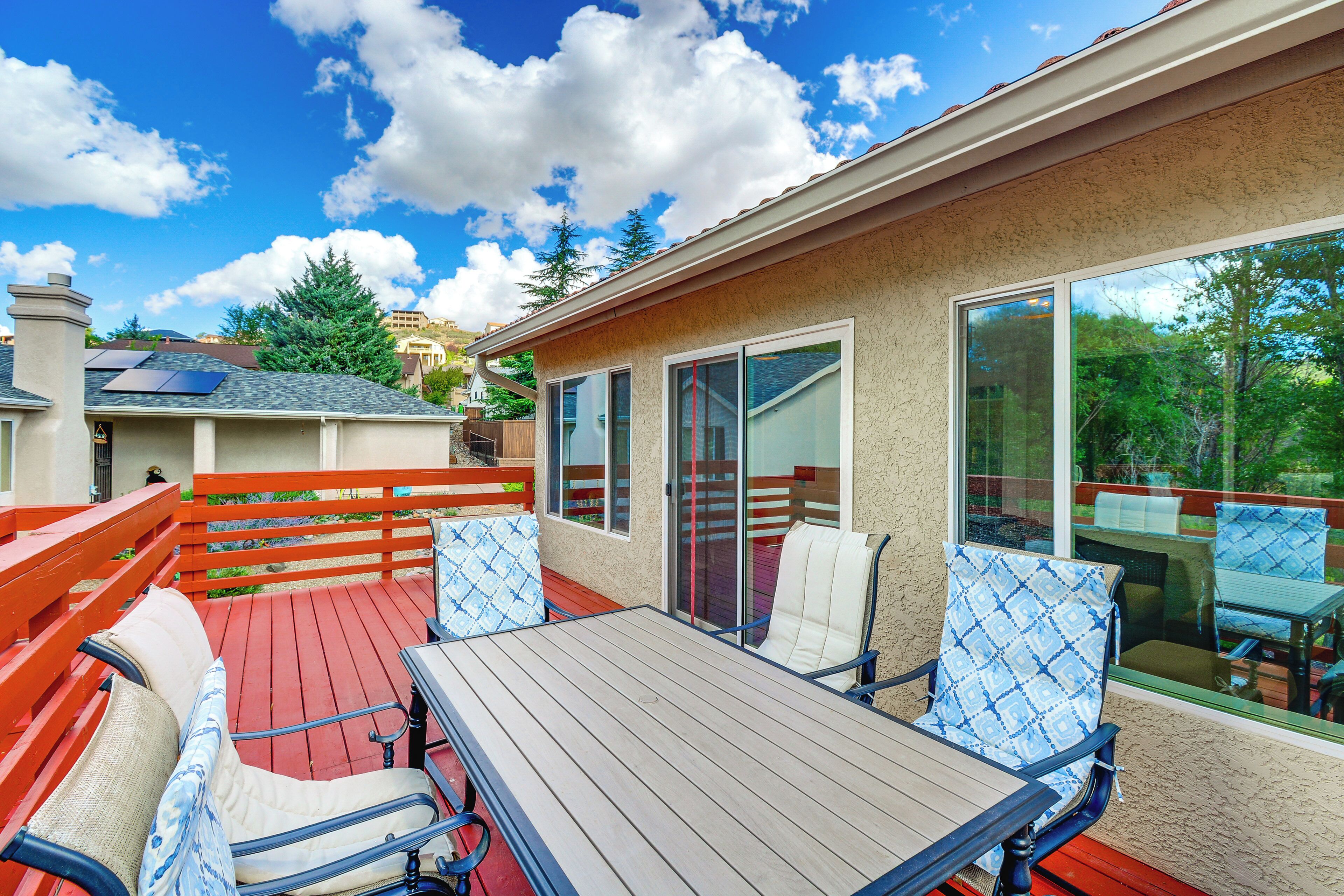 Eine überdachte Terrasse mit Holztisch und -stühlen, ein roter Deck und große Fenster mit Blick auf die Umgebung.