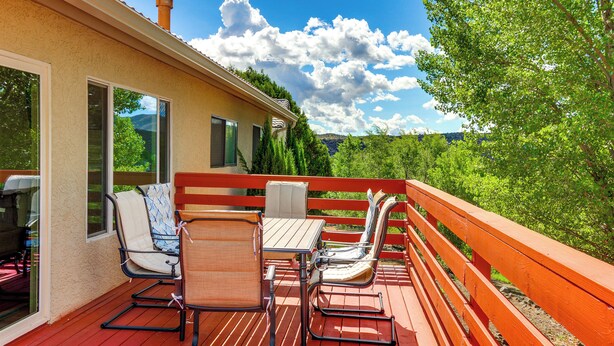 A wooden deck with outdoor furniture, including chairs and a table, overlooking a lush green landscape.