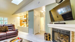 A living room with a fireplace, a leather sofa, a television, and a dining area with a basket and bowl.