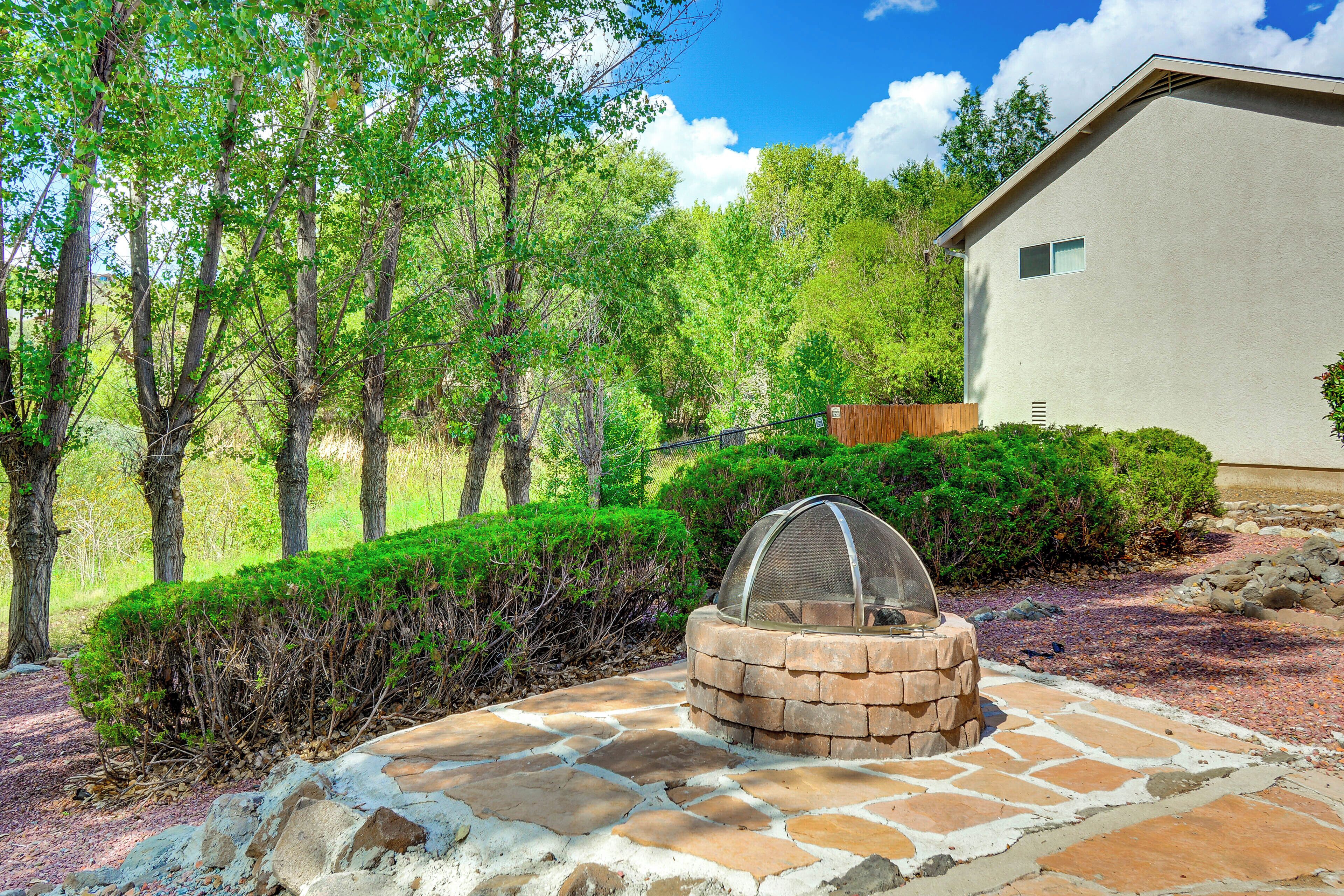 A stone patio with a fire pit, surrounded by lush greenery and trees.