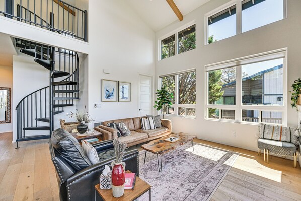 A spacious living room with a black leather sofa, a wooden coffee table, and a staircase with black railings.