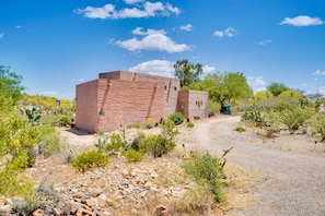Um edifício de tijolos com um caminho de terra que o leva, rodeado por vegetação do deserto.