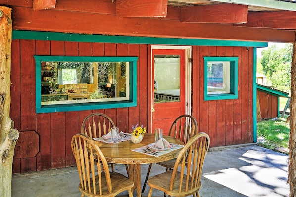 A wooden table with four chairs, a vase with flowers, and a window with a view of greenery.