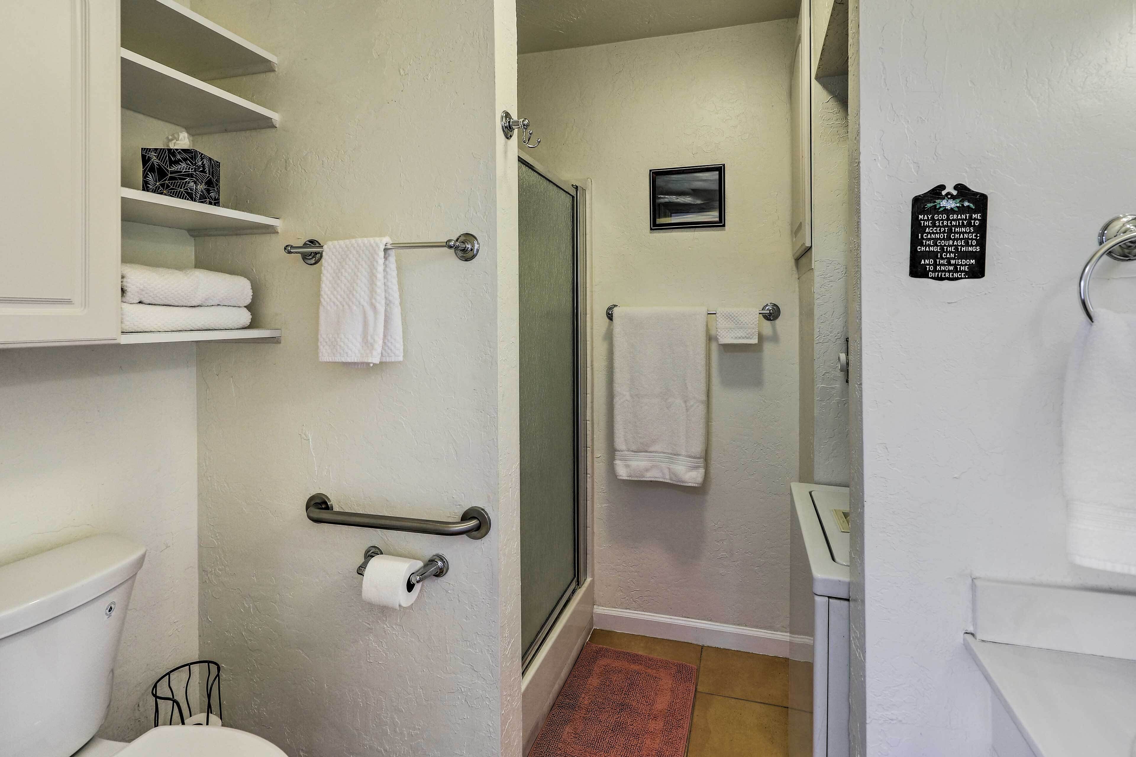 A bathroom with a toilet, a shower, and a sink. There are towels on the wall and a handrail.