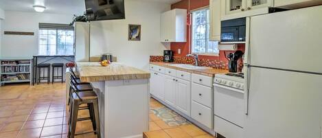 A kitchen with white cabinets, a stove, and a refrigerator. There is a window with a view of trees, and a ceiling fan.