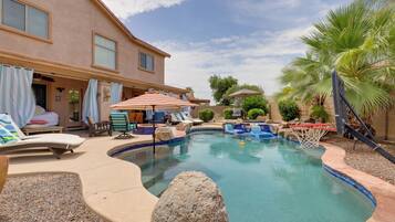 A swimming pool with lounge chairs, a basketball hoop, and a covered seating area.