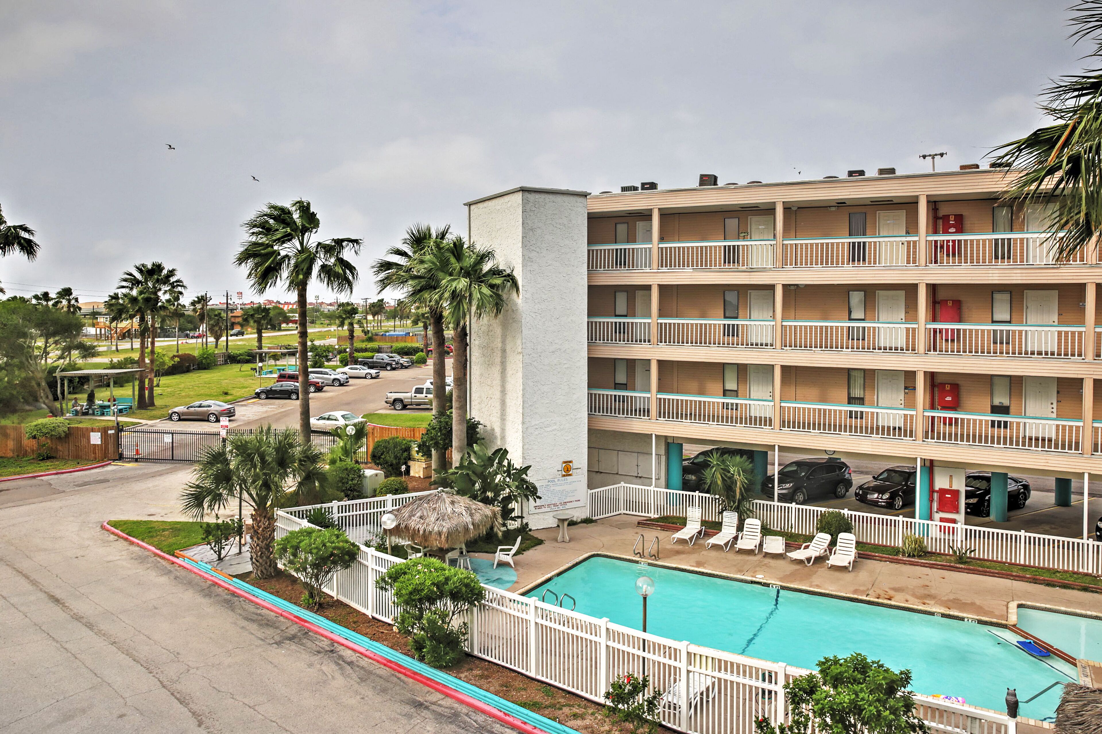 A multi-story hotel with a swimming pool, palm trees, and a parking lot.