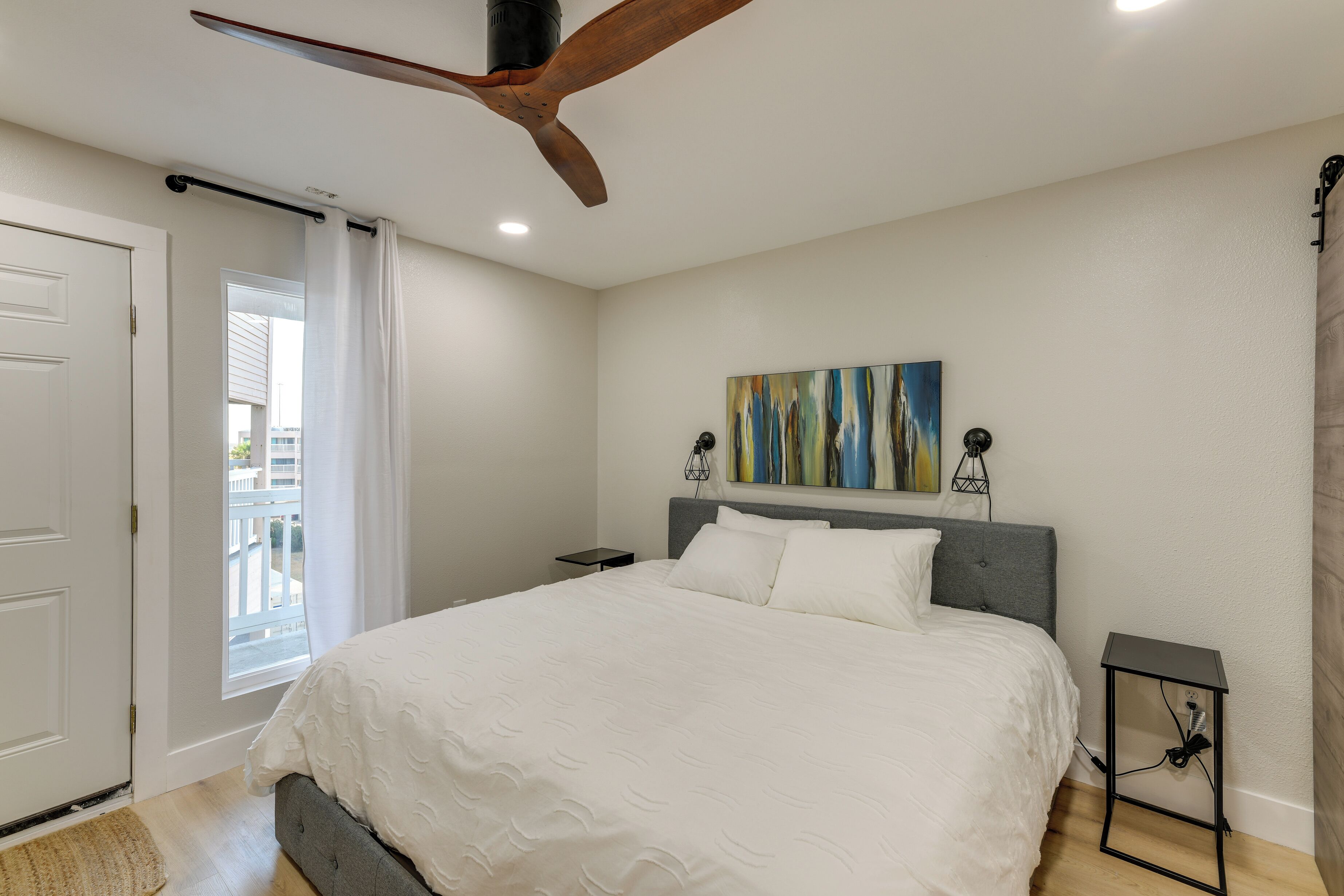 Un dormitorio con cama, ventilador de techo, un cuadro y una mesita de noche.