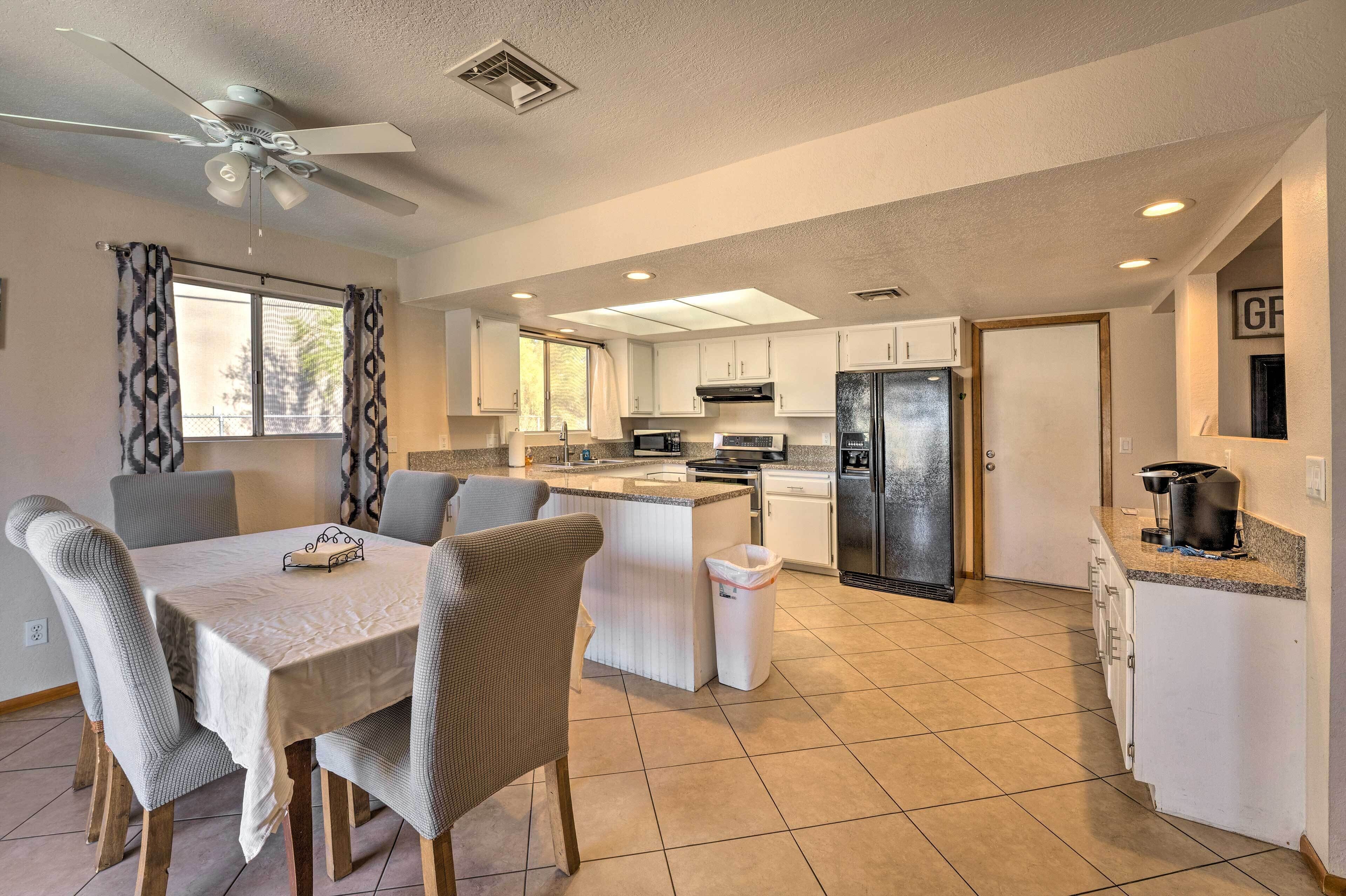 Una cocina moderna con comedor, que incluye una isla central, armarios blancos y un ventilador de techo.