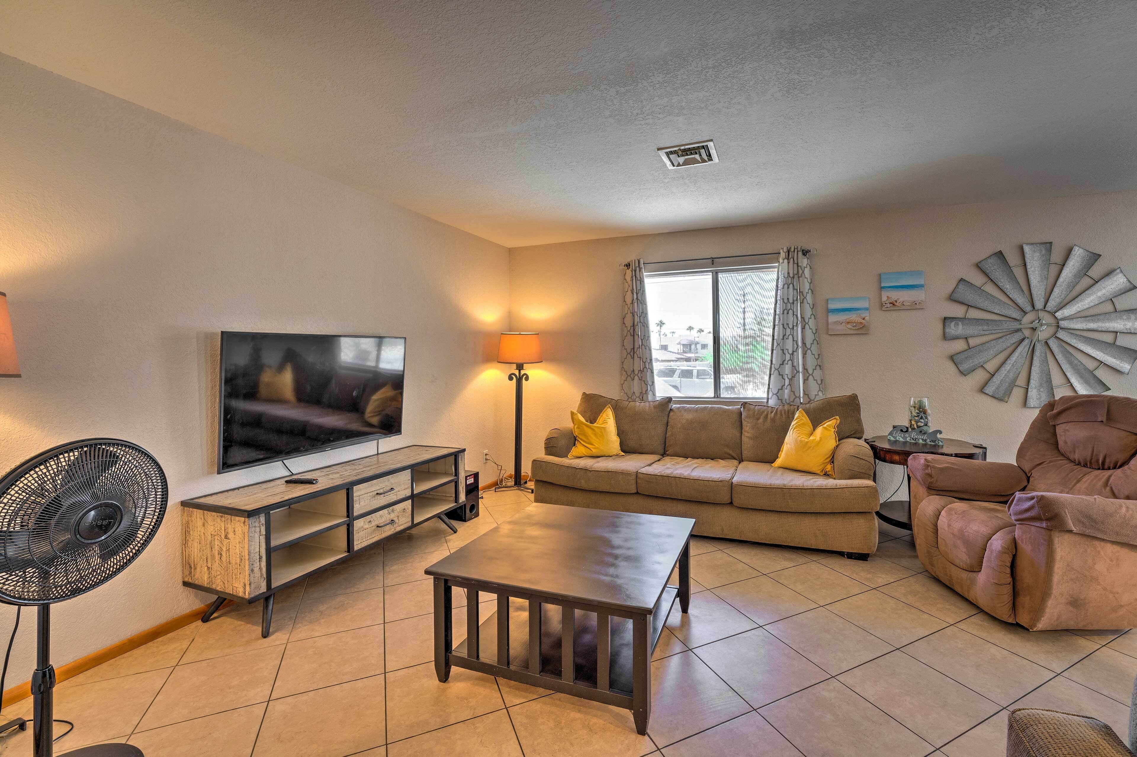 A living room with a TV, sofa, armchair, and a fan.